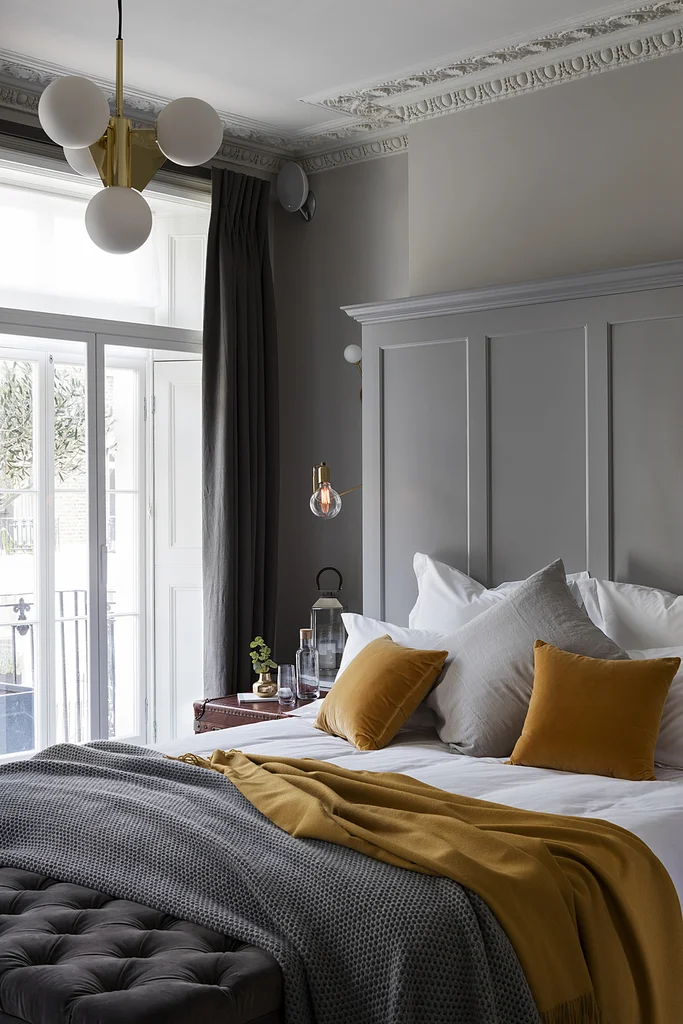 Light grey bedroom with warm mustard cushions and brass pendant light
